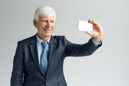 Business Lifestyle. Businessman standing isolated on gray taking selfie on smartphone smiling cheerfulの写真素材