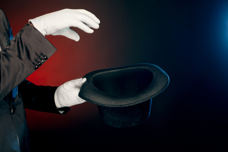 Professional Occupation. Showman in suit and gloves standing isolated on wall making tricks with hat close-upの写真素材