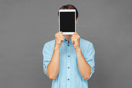 Freestyle. Teenager boy standing isolated on grey covering face with digital tabletの写真素材