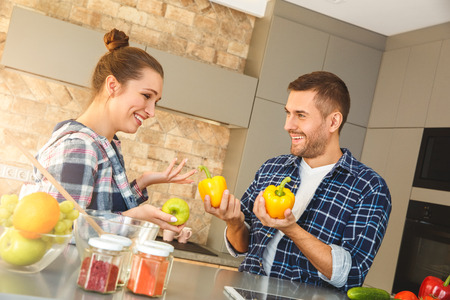 Young couple at home standing in kitchen together playing with vegetables cheerfulの写真素材