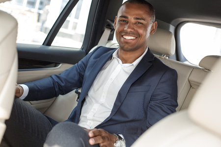 Young businessman sitting on back seat in car smiling joyfulの写真素材