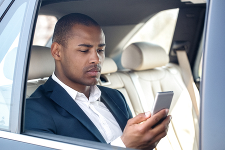 Young businessman sitting in car window opened reading message on smartphone seriousの写真素材