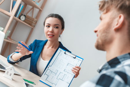 Man at real estate agency sitting agent explaining layout to clientの写真素材