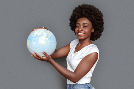 Young woman standing isolated on gray with globe looking camera joyful traveling around worldの写真素材