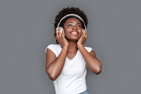 Young woman in headphones standing isolated on gray listening music looking up inspiredの写真素材