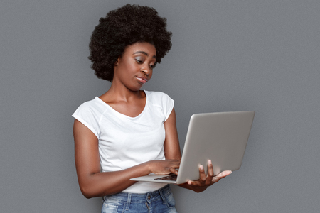 Young woman standing isolated on gray working on laptop concernedの写真素材