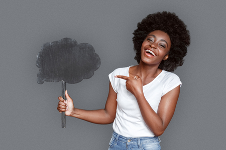 Young woman standing isolated on gray pointing at cloud laughing cheerfulの写真素材