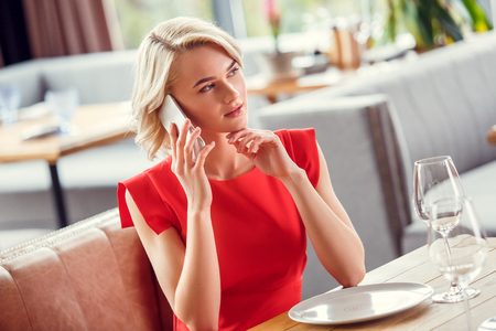 Young woman dining in restaurant sitting talking on smartphone thoughtfulの写真素材