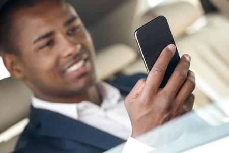 Young businessman sitting in the car playing game on smartphone joyful close-up blurred backgroundの写真素材
