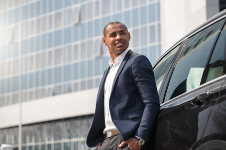 Young man standing near car hands in pockets looking aside pensive side viewの写真素材
