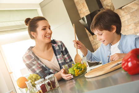 Family at home standing in kitchen together son mixing salad helping mom cheerful close-upの写真素材