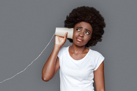 Young woman standing isolated on gray listening conversation paper telephone unsatisfiedの写真素材
