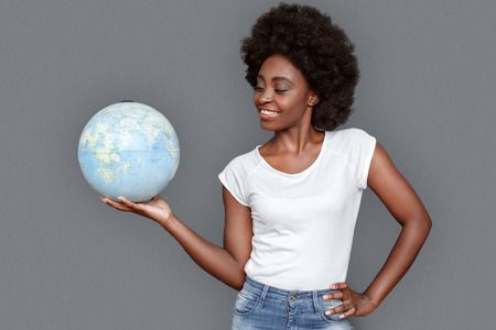 Young woman standing isolated on gray with globe looking at destination excitedの写真素材