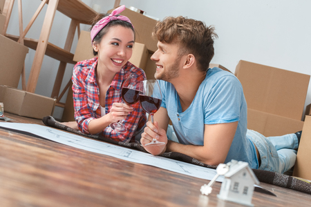 Young couple moving to new place lying cheers with glasses of wine talking joyfulの写真素材