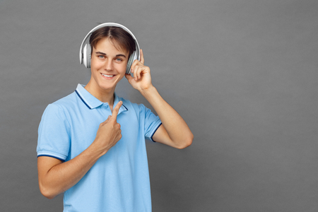 Freestyle. Teenager boy pointing up at headphons standing isolated on grey listening music smiling playfulの写真素材