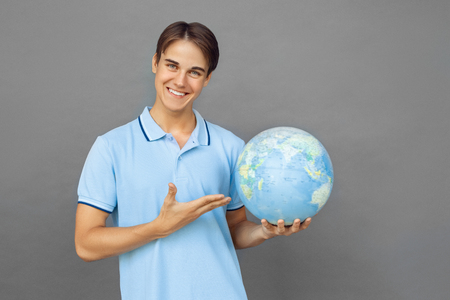 Freestyle. Teenager boy standing isolated on grey showing globe smiling friendlyの写真素材