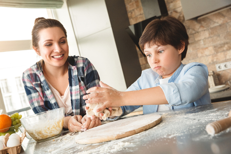 Family at home standing at table in kitchen together son kneading dough while mother looking at him happyの写真素材