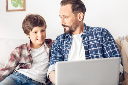 Father and little son at home sitting on sofa using laptop joyful close-upの写真素材