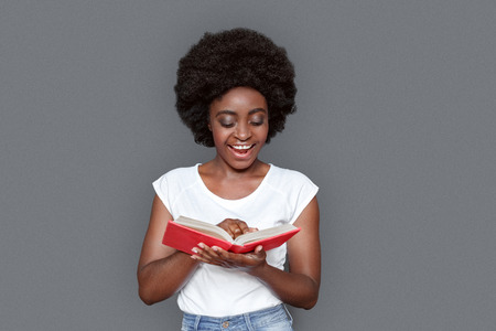 Young woman standing isolated on gray reading story smiling excitedの写真素材