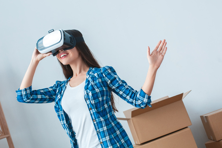 Young brunette woman moving to a new place standing wearing virtual reality headset moving smiling playfulの写真素材