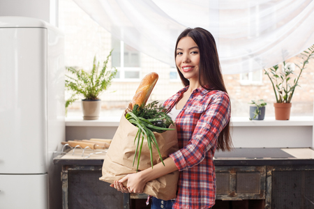 Young girl at kitchen healthy lifestyle standing holding bag with purchases looking camera happyの写真素材