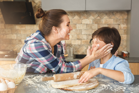 Family at home standing at table in kitchen together mother touching sons face with floured hands smiling happyの写真素材