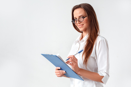 Business lifestyle. Woman in eyeglasses standing isolated on white with clipboard taking notes smiling playfulの写真素材