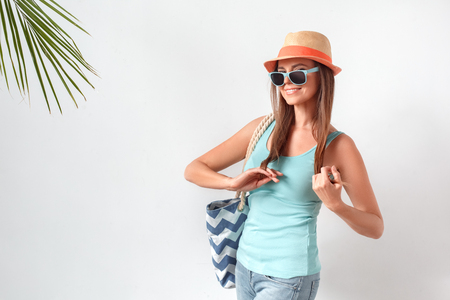 Summertime. Woman in hat and sunglasses standing studio isolated on white with beach bag posing to camera playfulの写真素材
