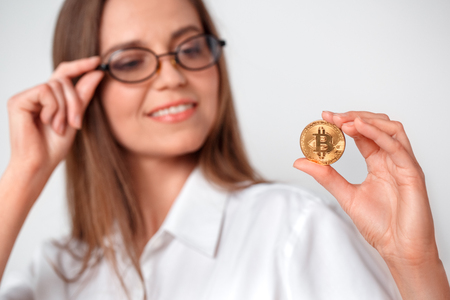 Electronic cash. Woman in eyeglasses standing isolated on white looking at cryptocurrency curious close-upの写真素材