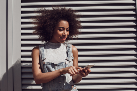 Young woman wearing overall shorts isolated on shutter browsing smartphone joyfulの写真素材