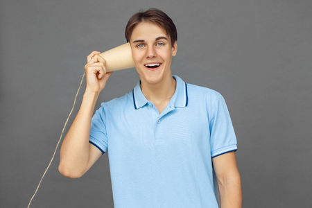 Freestyle. Teenager boy standing isolated on grey listening string telephone looking camera surprisedの写真素材