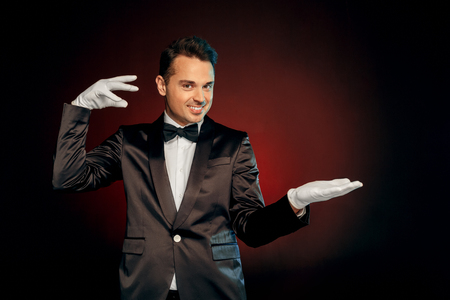 Professional Occupation. Showman in suit and gloves standing isolated on wall showing trick looking camera playfulの写真素材