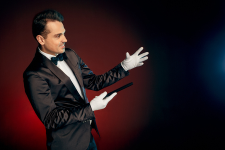 Professional Occupation. Showman in suit standing isolated on wall making trick with cane smiling happyの写真素材