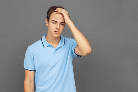 Freestyle. Teenager boy standing isolated on grey touching head concernedの写真素材