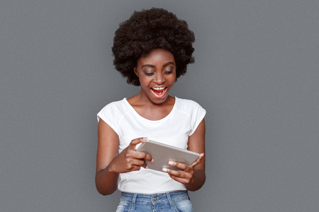 Young woman standing isolated on gray playing game on digital tablet cheerfulの写真素材