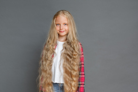 Little girl standing isolated on grey showing long hair looking camera relaxedの写真素材