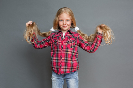 Little girl with ponytails standing isolated on grey looking camera playfulの写真素材