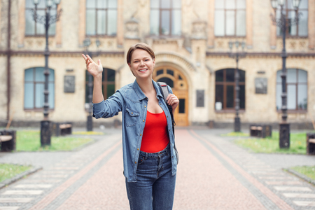 Young student with backpack at university campus standing waving to camera happyの写真素材