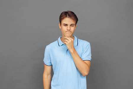 Freestyle. Teenager boy standing isolated on grey touching chin thoughtfulの写真素材