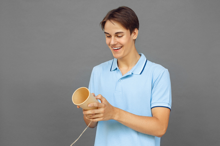 Freestyle. Teenager boy standing isolated on grey looking at string telephone excitedの写真素材