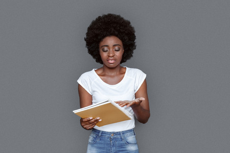 Young woman standing isolated on gray looking at notebooks concernedの写真素材