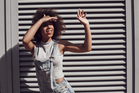 Young woman wearing overall shorts isolated on shutter hiding from sun looking aside dreamfulの写真素材