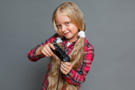 Little girl with ponytails standing isolated on grey playing game console excitedの写真素材