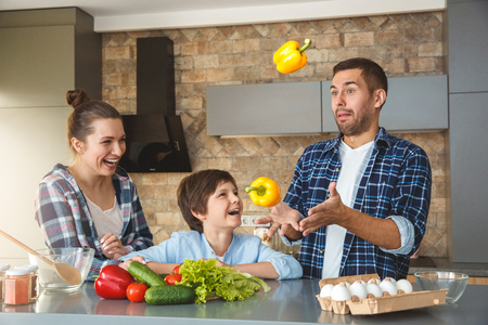 Family at home standing in kitchen together mother and son looking at father juggling laughing joyfulの写真素材