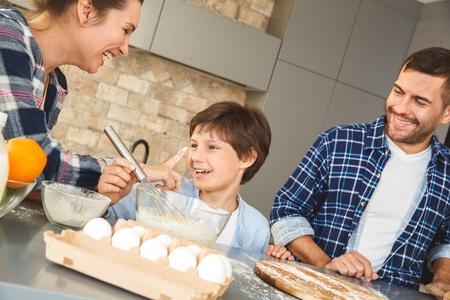 Family at home standing at table in kitchen together mother touching son with hands dirty in flour laughing cheerfulの写真素材
