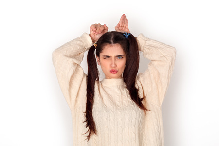 Young girl with two ponytails studio standing isolated on white showing rabbit winking playfulの写真素材