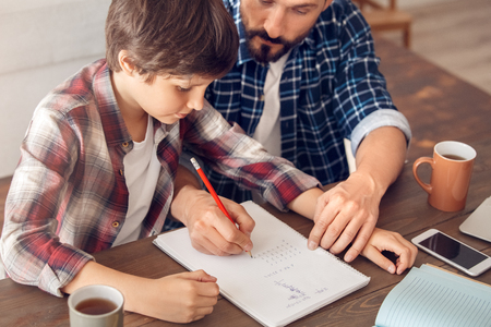 Father and son at home sitting at table dad showing boy how to do math exercise close-upの写真素材
