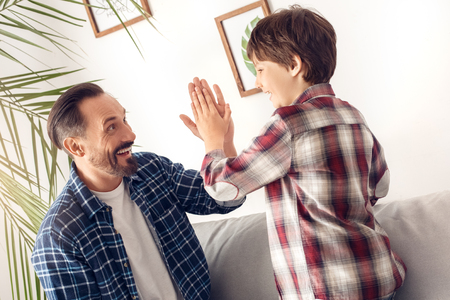 Father and little son at home sitting on sofa giving high five looking at each other cheerful close-upの写真素材