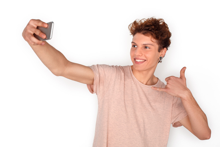 Teenager with earrings studio standing isolated on white taking selfie on smartphone showing call gesture playfulの写真素材