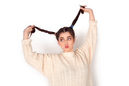 Young woman studio standing isolated on white holding ponytails up pouting lips childishの写真素材